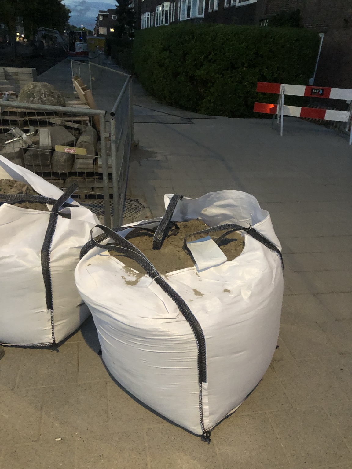 Twee witte bigbags naast bouwhekken; rechts daarvan blijft het trottoir open