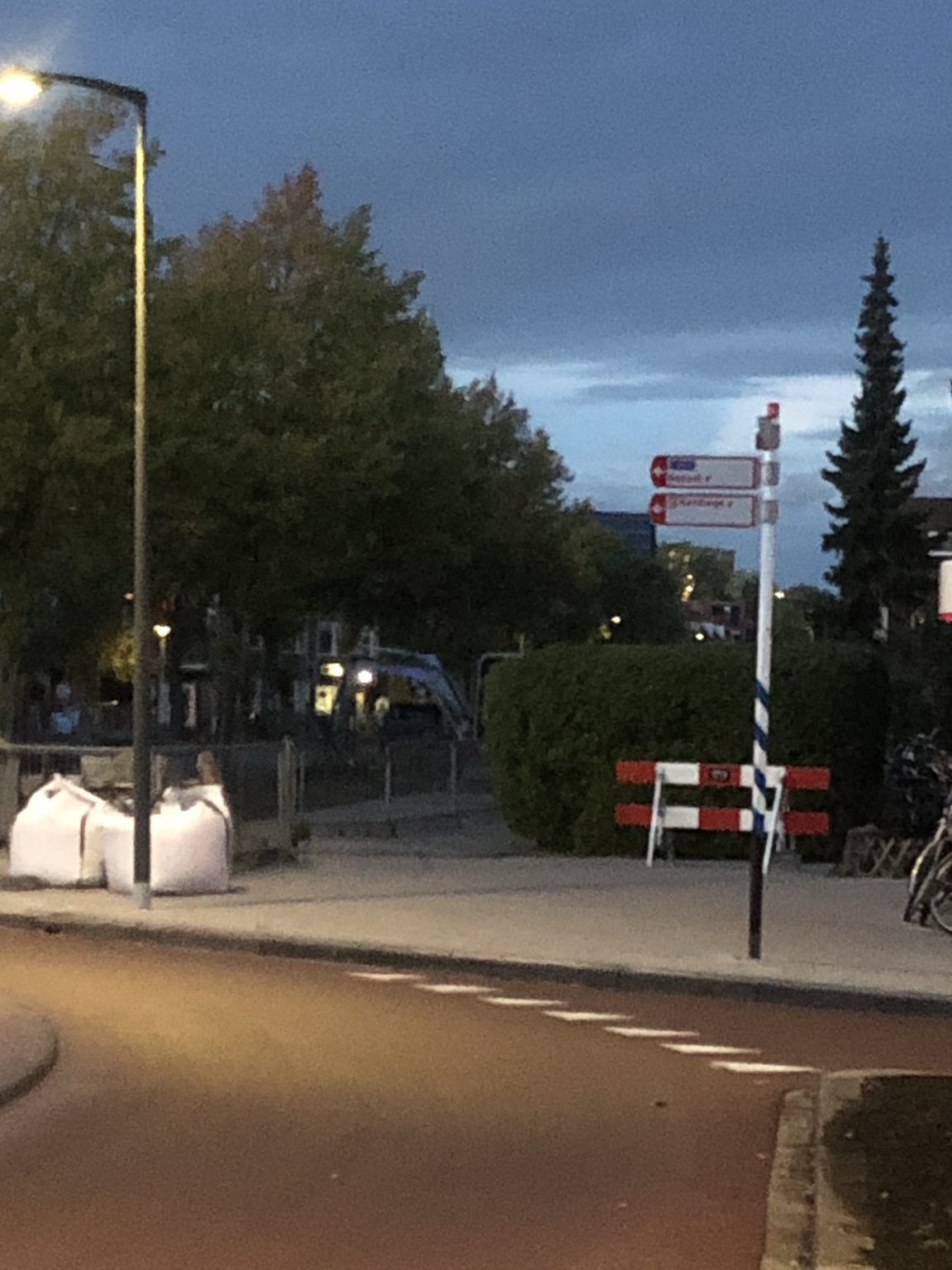 Overzicht vanaf de rotonde: bigbags links en een rood-wit hek rechts, met een open doorgang naar het trottoir